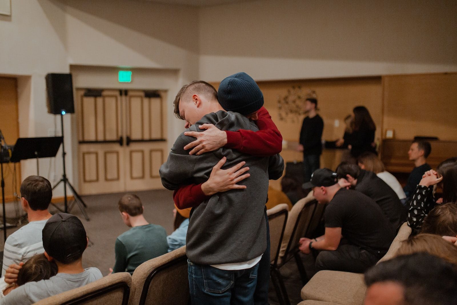 Two people embracing in a warmly lit room with an audience.