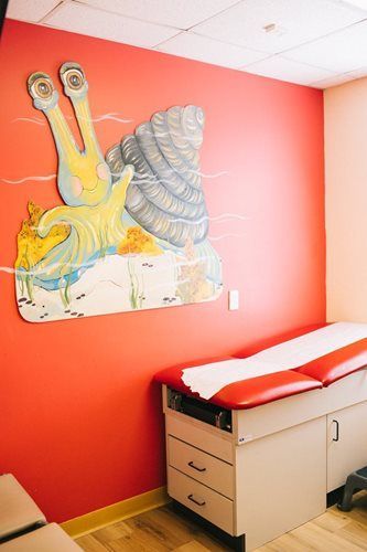 Examination room with snail mural, red wall, medical table.