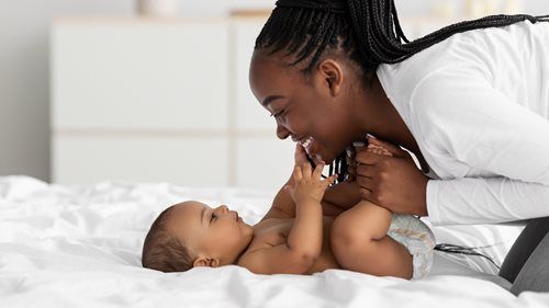Woman smiling, playing with baby on a white bed.