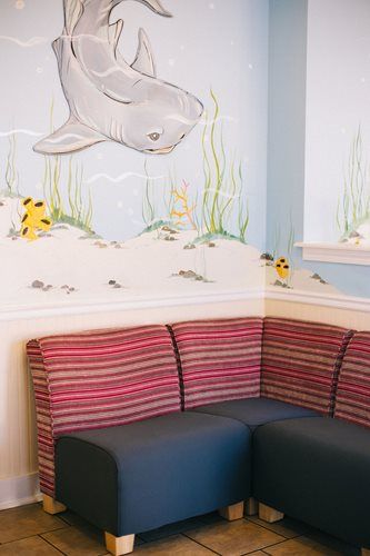 L-shaped bench with striped back and black seat in front of a painted ocean-themed wall with a shark.