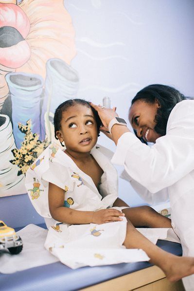 Doctor examining a child's ear with an otoscope in a doctor's office. The child looks apprehensive.