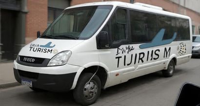 Minibús blanco con el logotipo de “Turismo” estacionado en una calle, vista lateral.