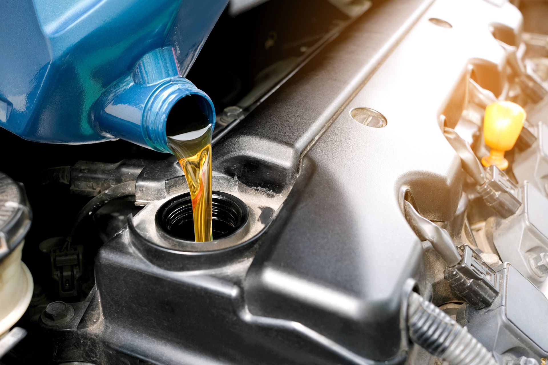 Blue engine oil being poured into a car’s oil filler cap under the hood.