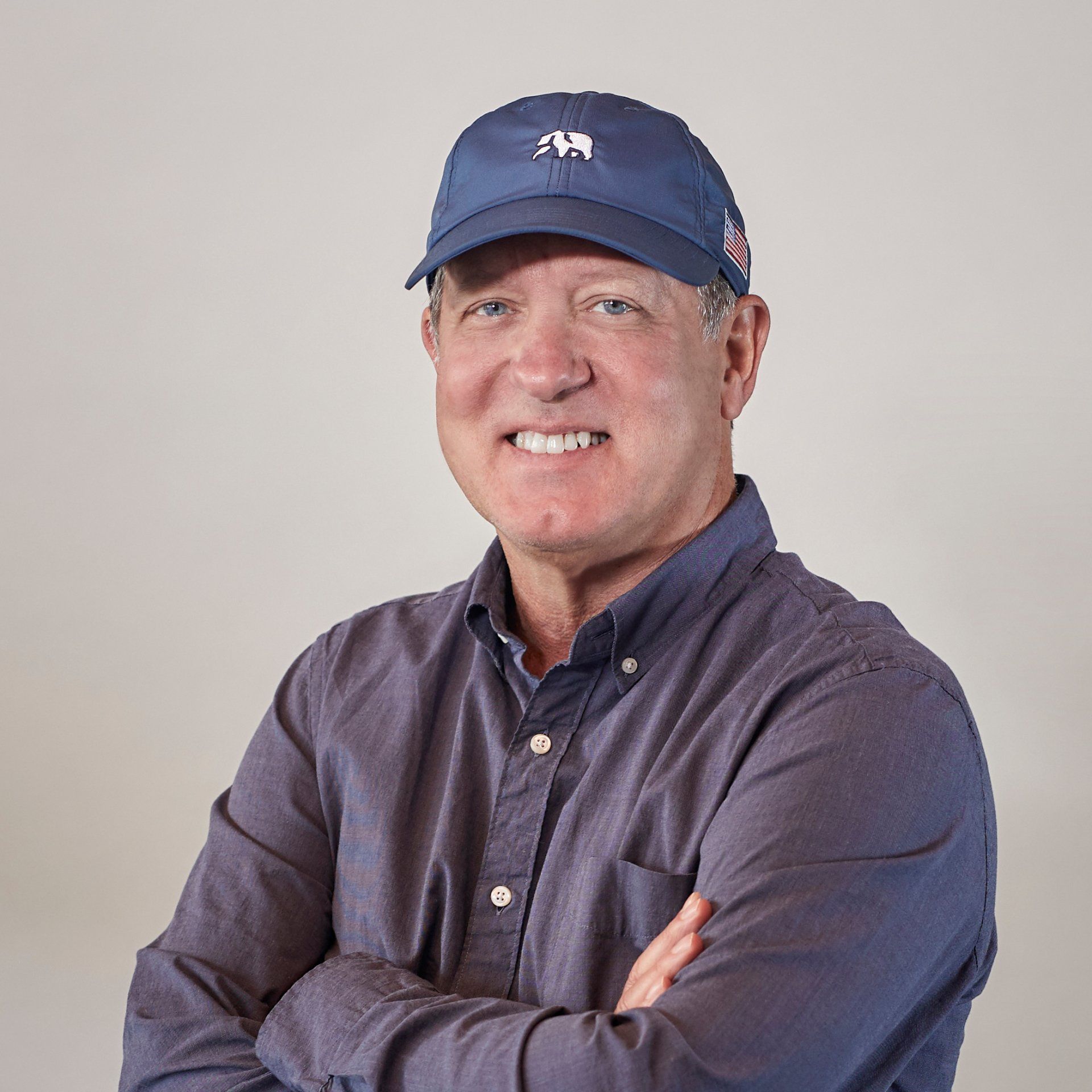 A man wearing a blue hat and a gray shirt is standing with his arms crossed.