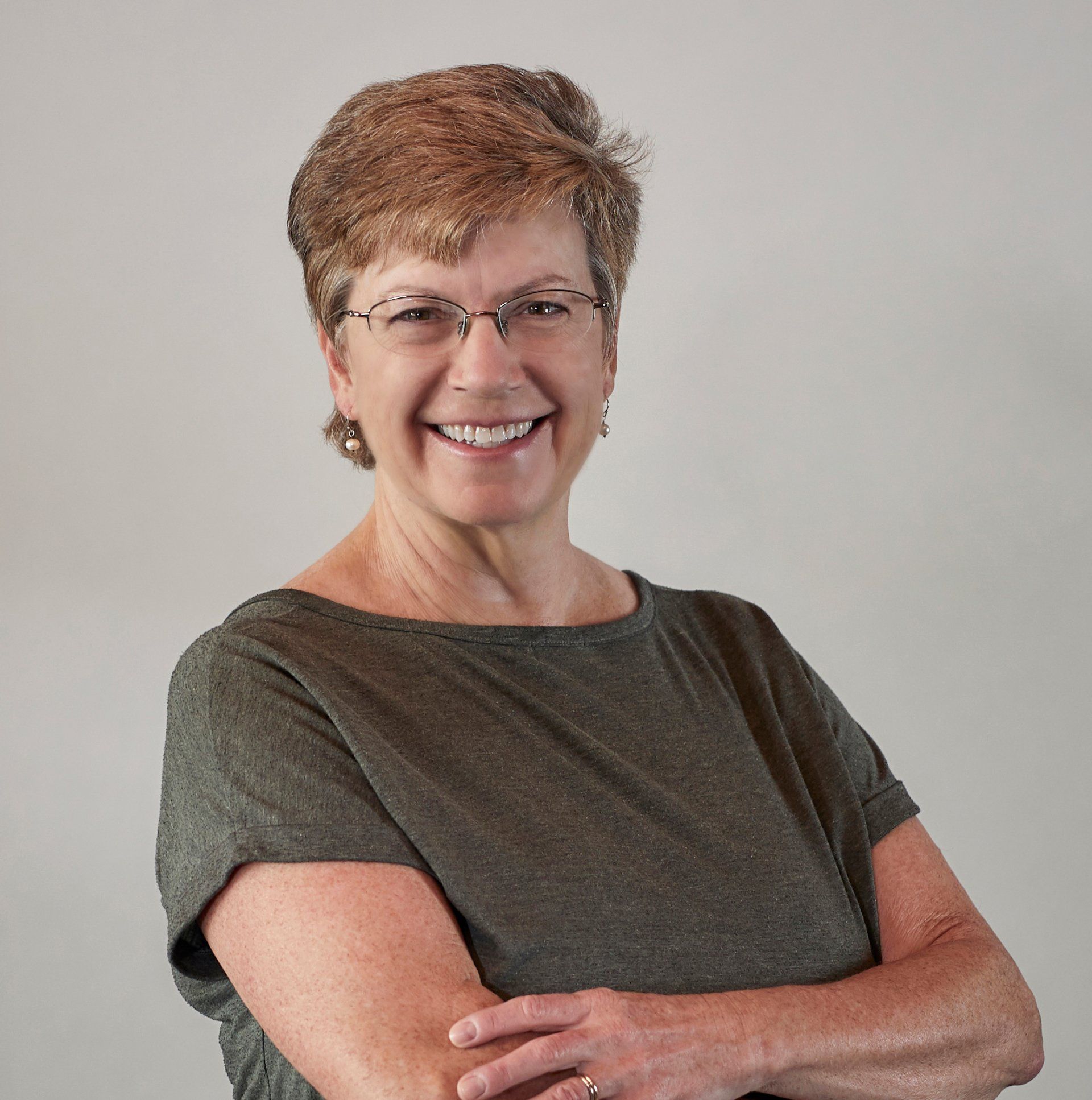 A woman wearing glasses is smiling with her arms crossed