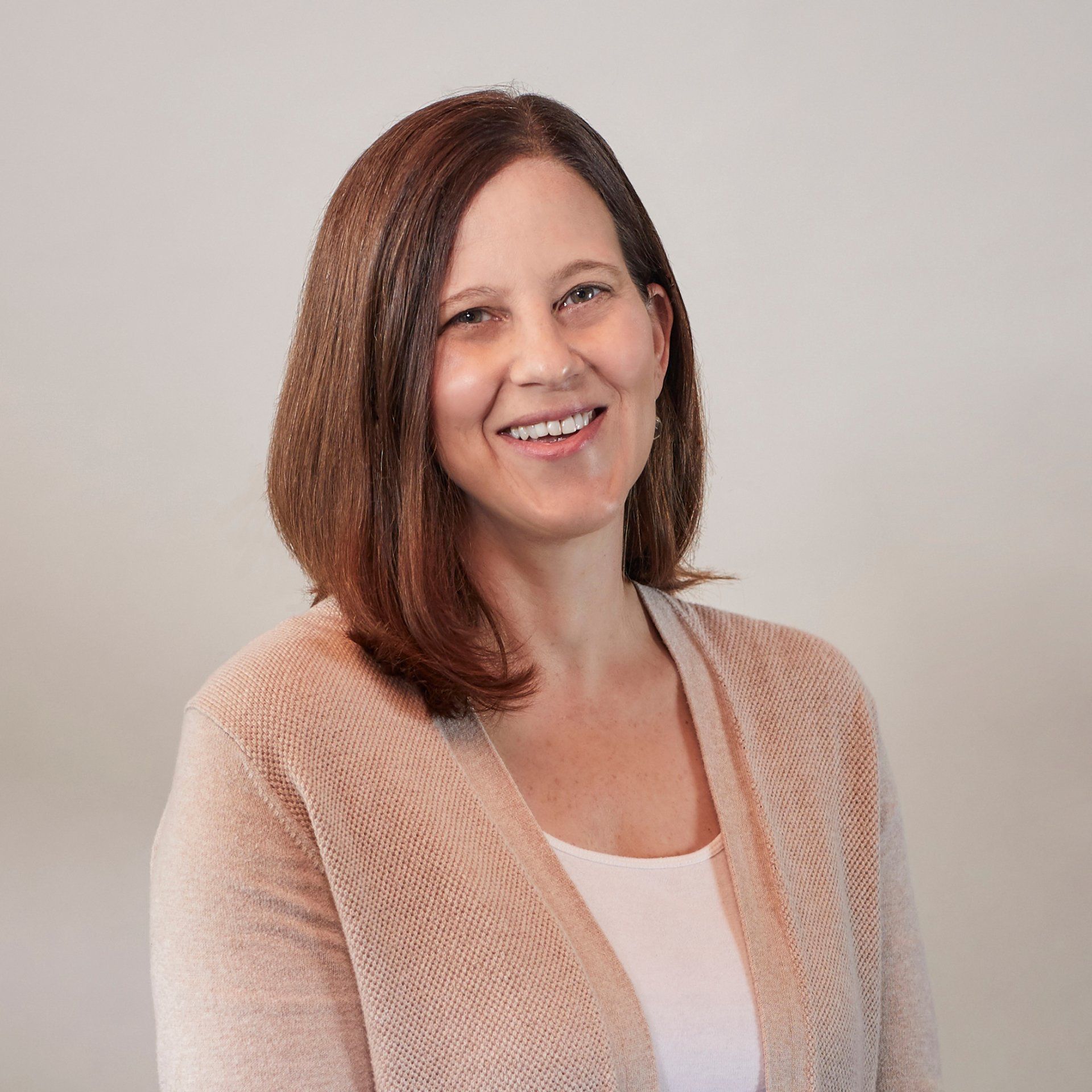 A woman wearing a sweater and a white shirt is smiling for the camera.