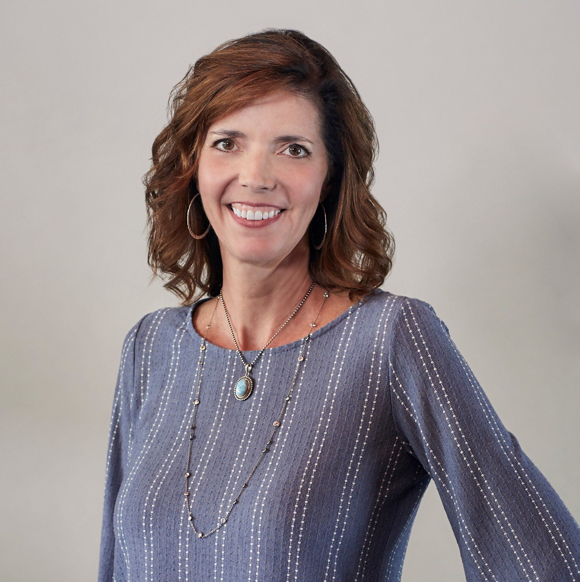 A woman wearing a blue striped shirt and a necklace smiles for the camera.