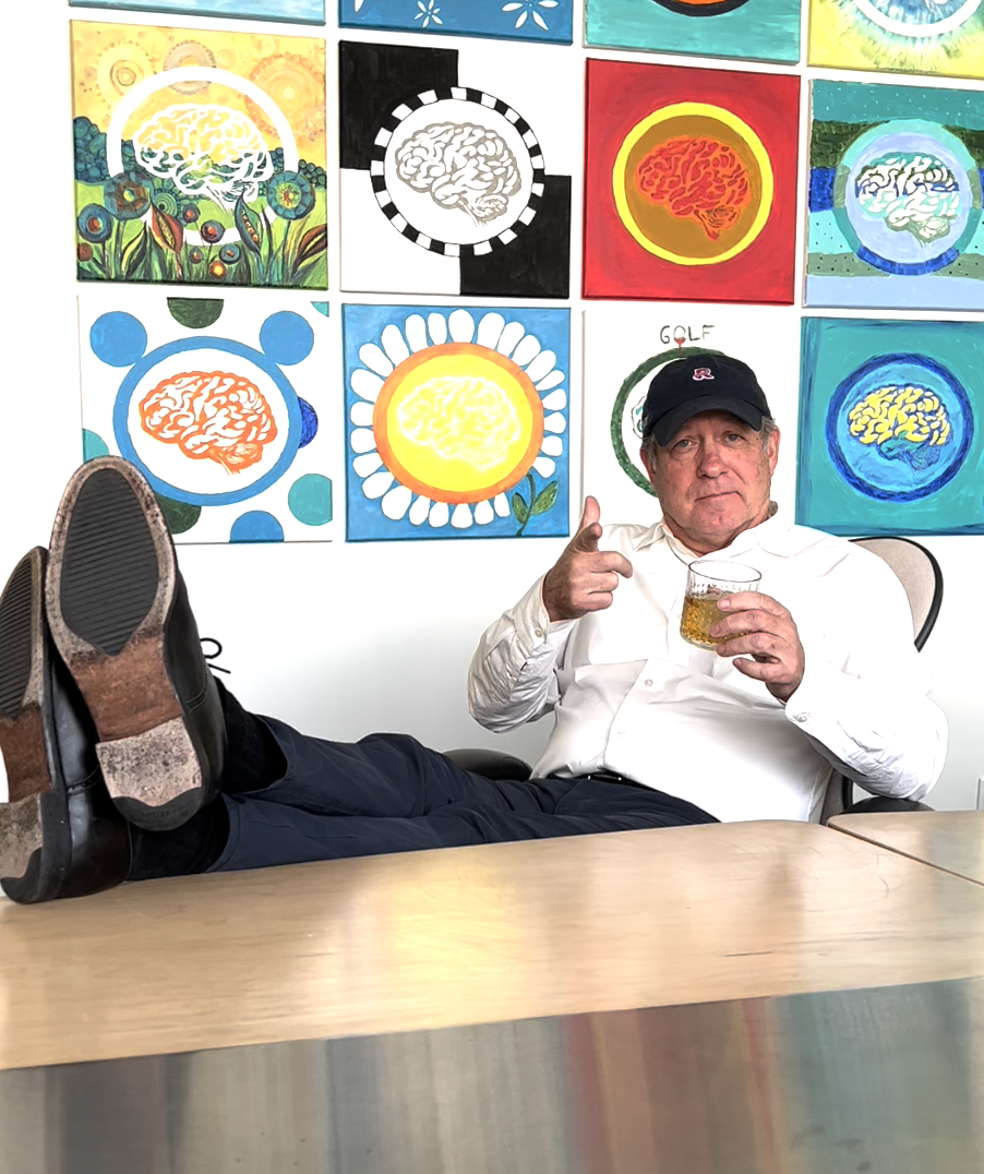 A man is sitting at a table with his feet up holding a glass of beer.