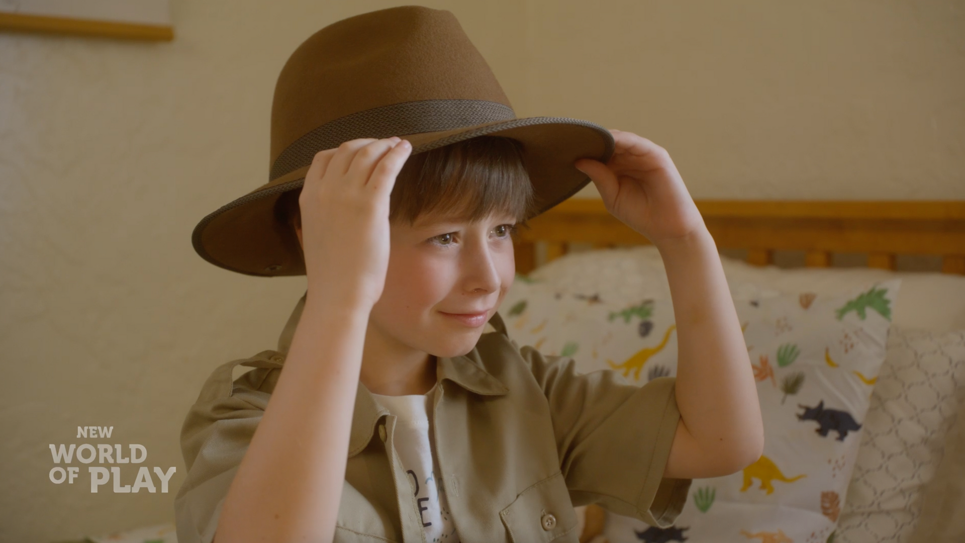 A young boy wearing a hat is sitting on a bed.