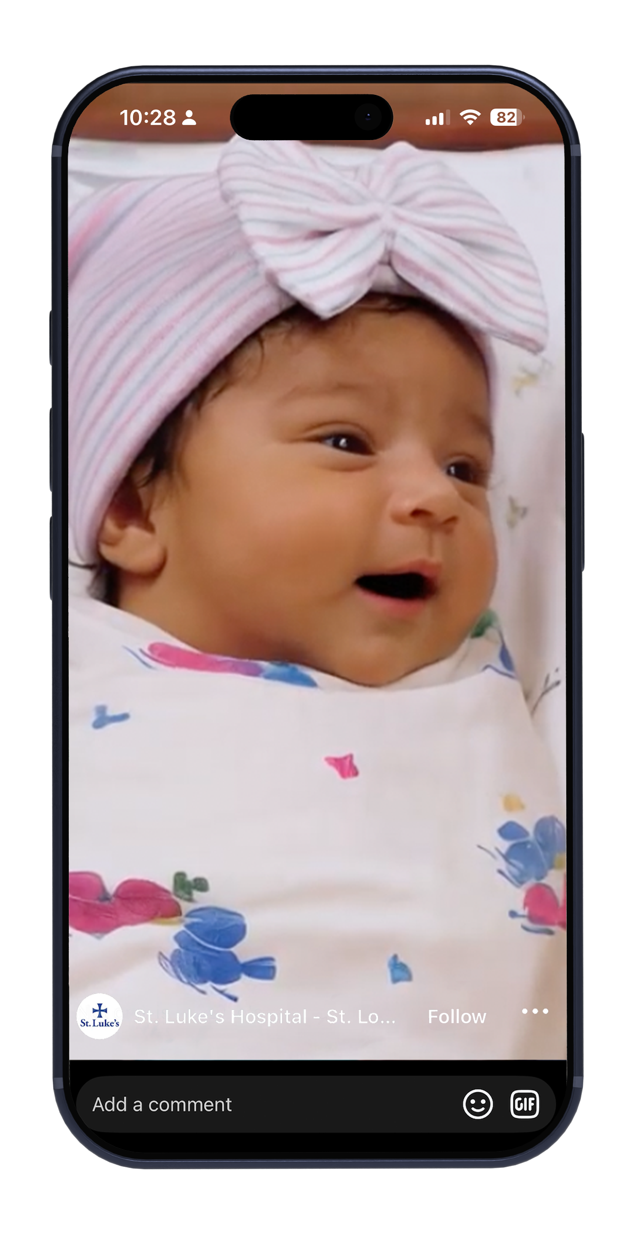 Baby in pink headwrap and floral outfit, smiling on a phone screen.