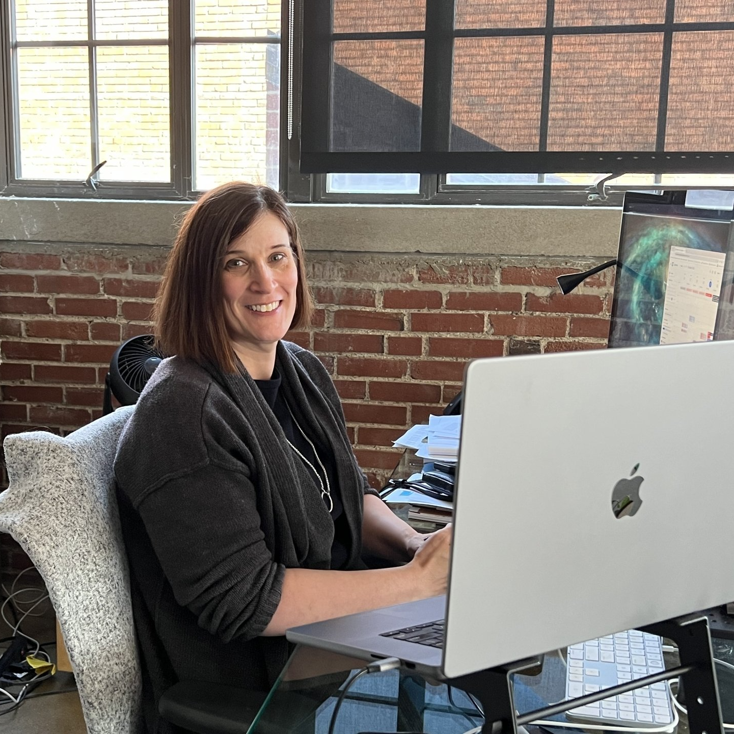 A woman is sitting at a desk in front of an apple laptop computer.