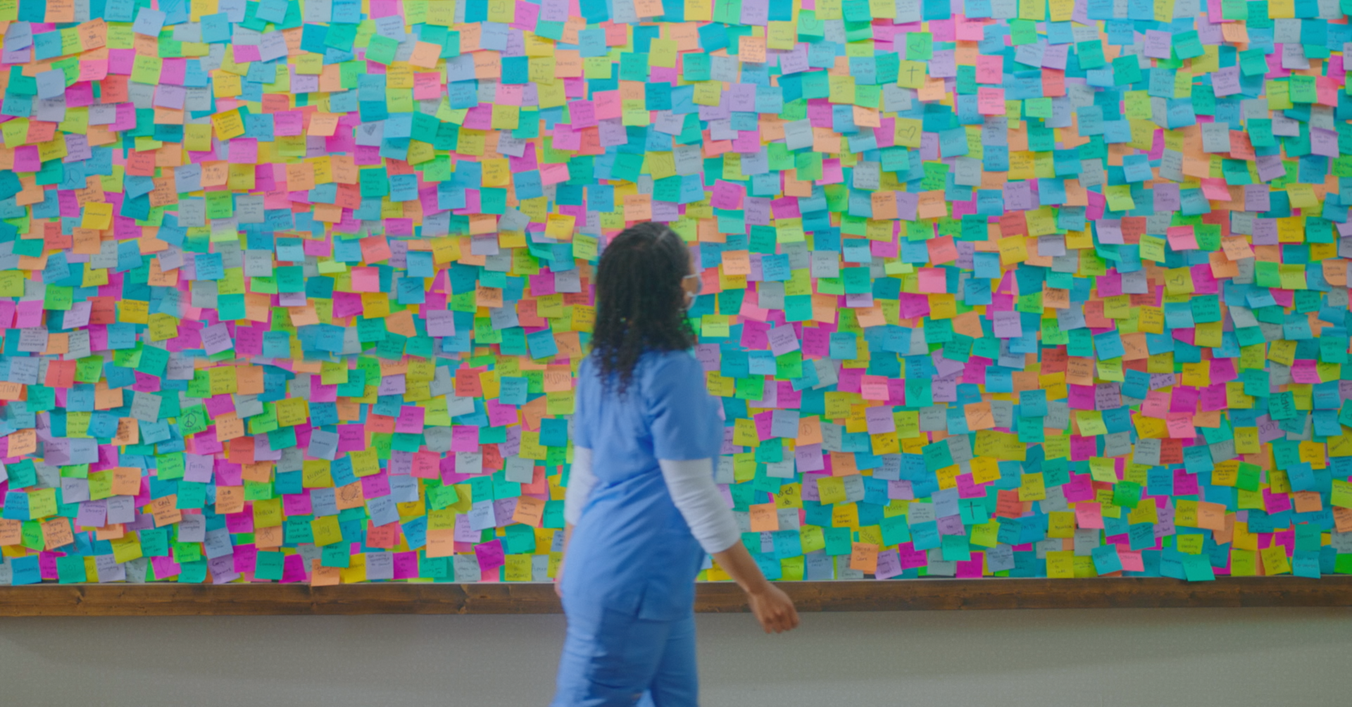 An Ascension nurse is standing in front of a wall covered in sticky notes.