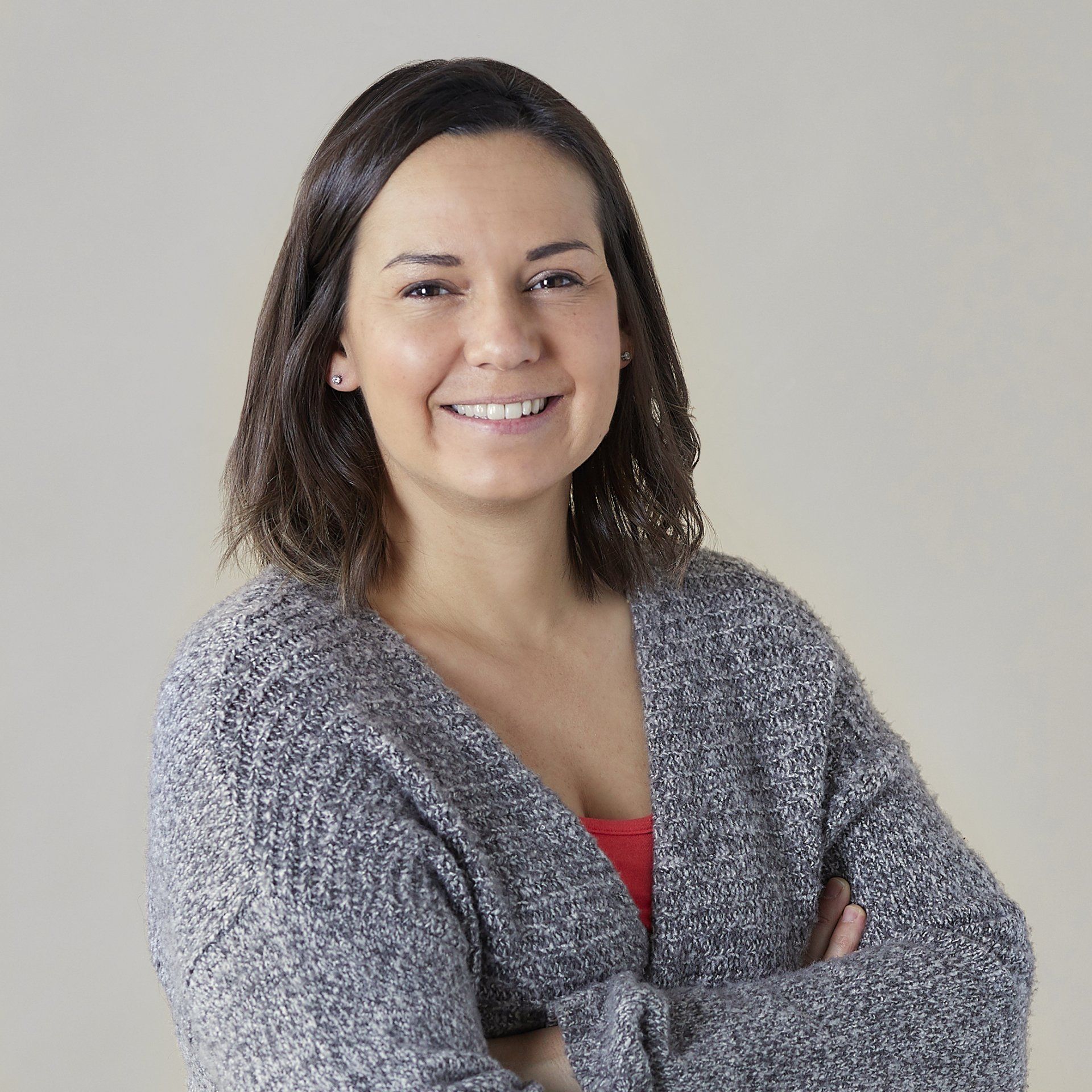 A woman in a grey sweater is smiling with her arms crossed