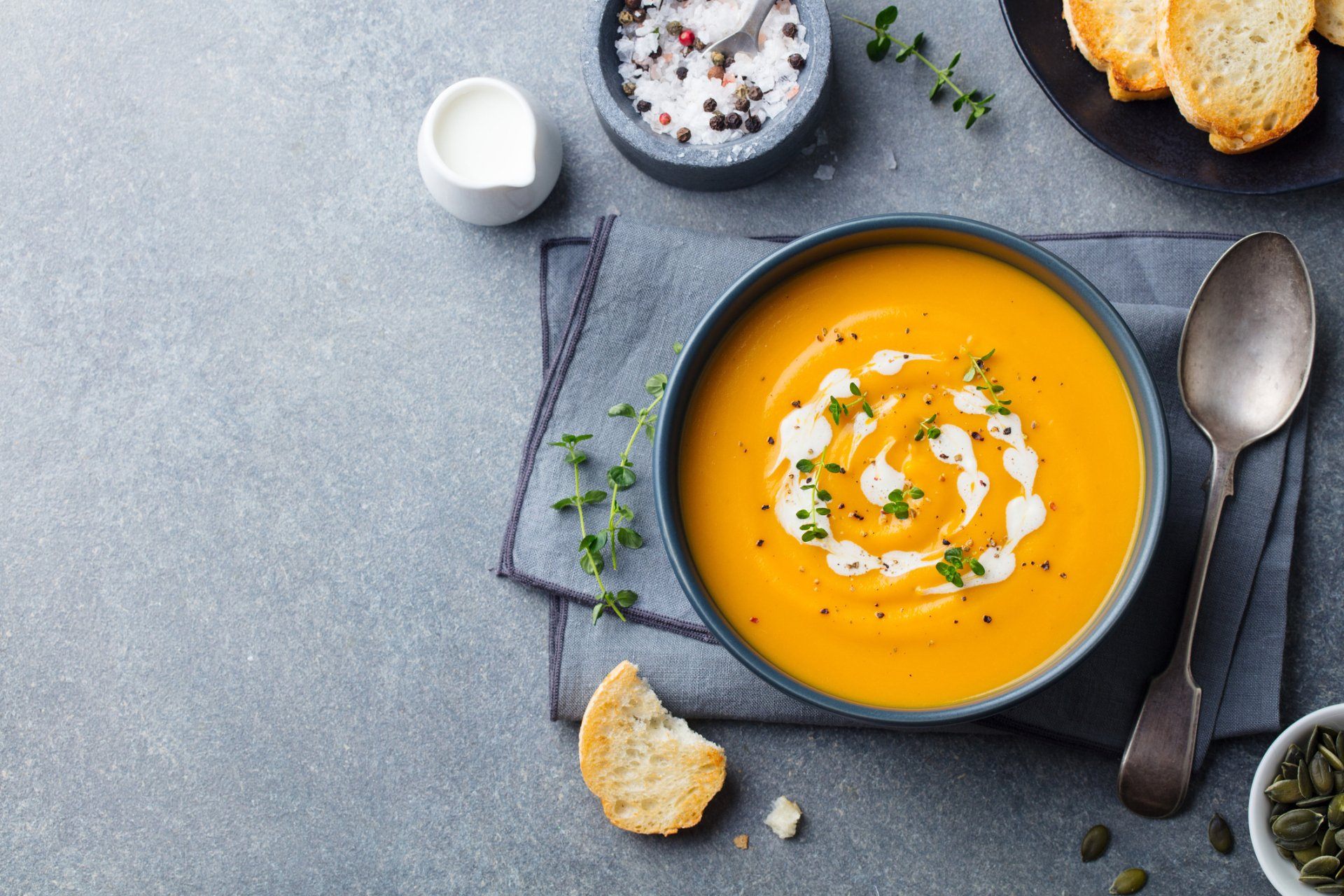 A bowl of pumpkin soup with whipped cream and croutons on a table.