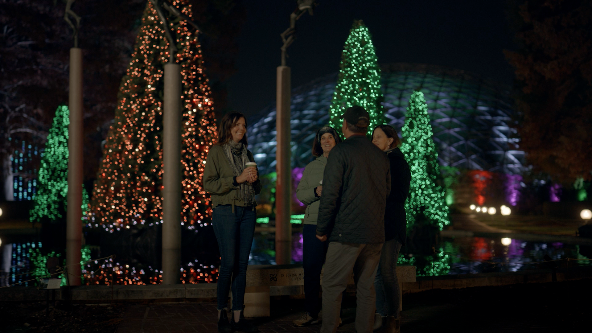 A group of people are standing in front of a christmas tree at night.