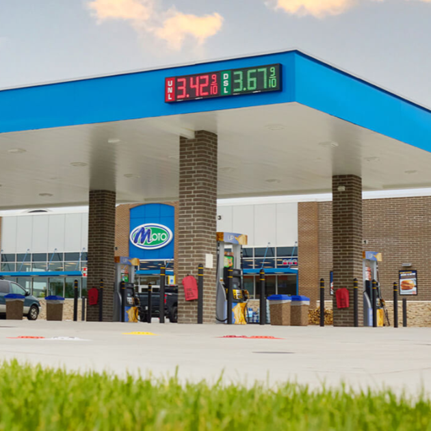 Moo gas station canopy with digital price sign and pumps, viewed from the forecourt.