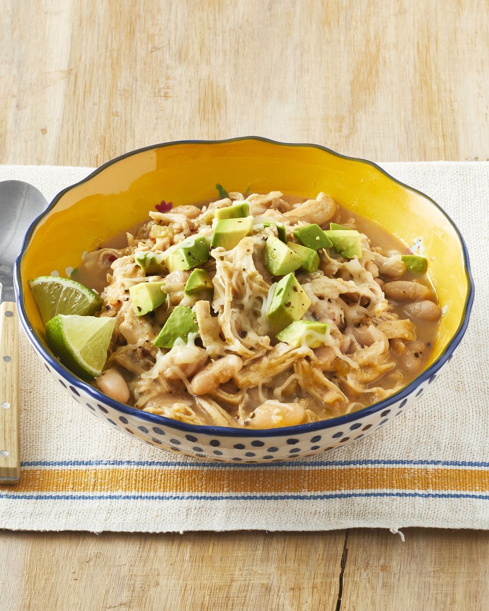 A bowl of soup with beans and avocado on a table with a spoon