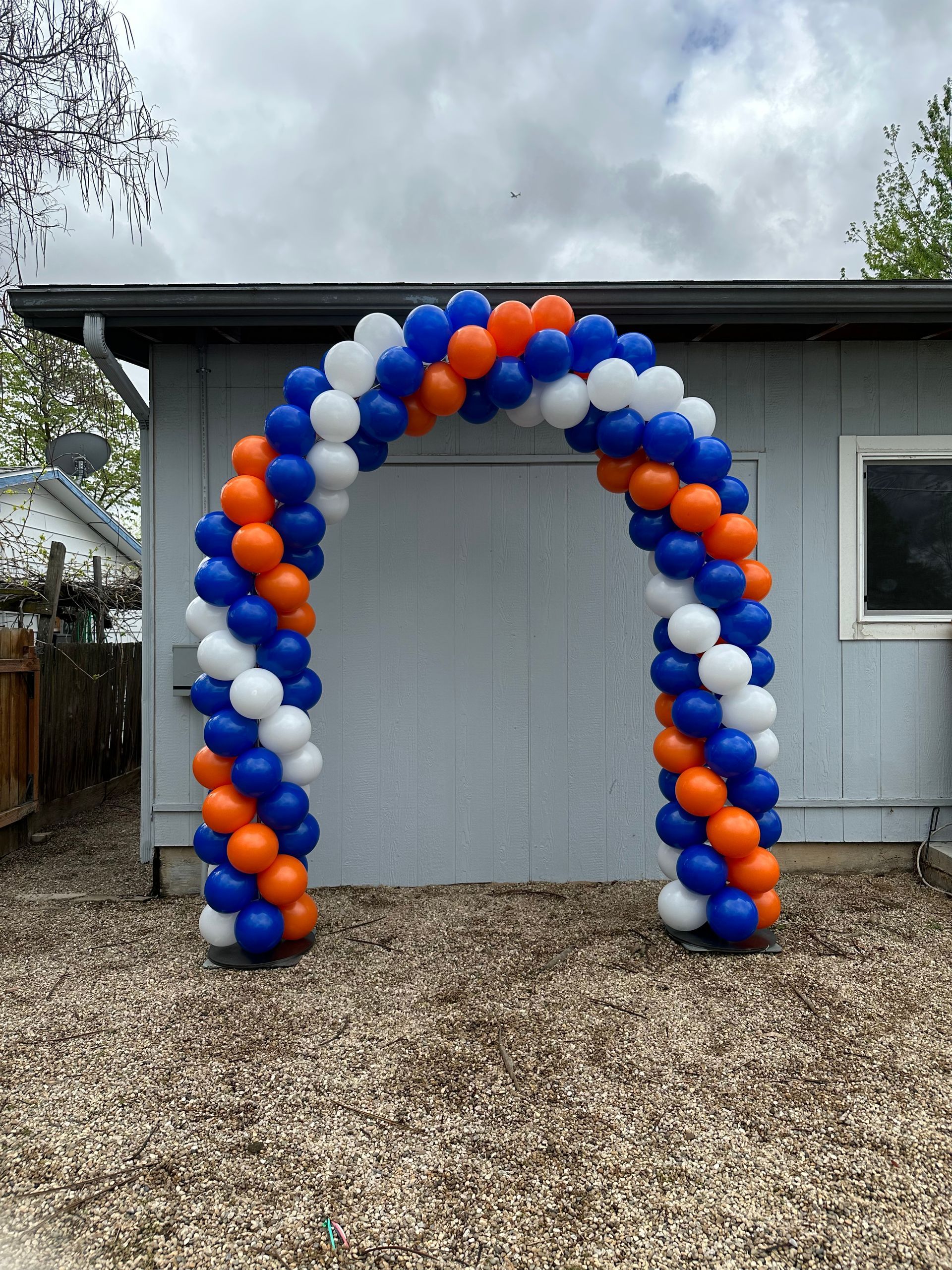 A blue , white and orange balloon arch is in front of a house.