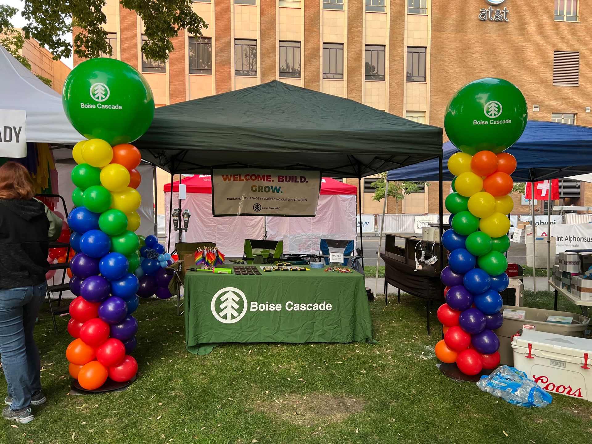 A man is standing in front of a tent decorated with rainbow colored balloons.