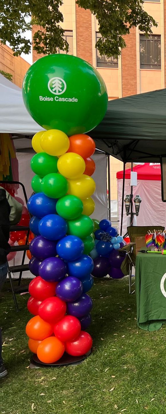 A rainbow colored balloon tower with a green balloon in the middle.