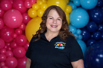 A woman in a blue shirt is standing in front of balloons.