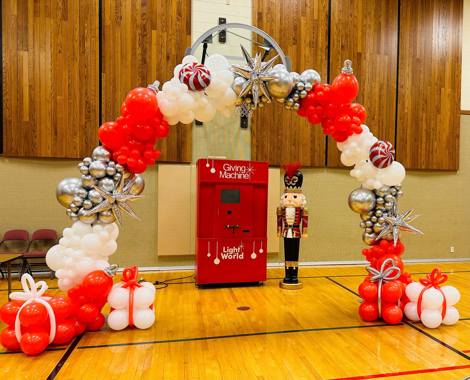A red and white balloon arch in a gym with a nutcracker in the background.