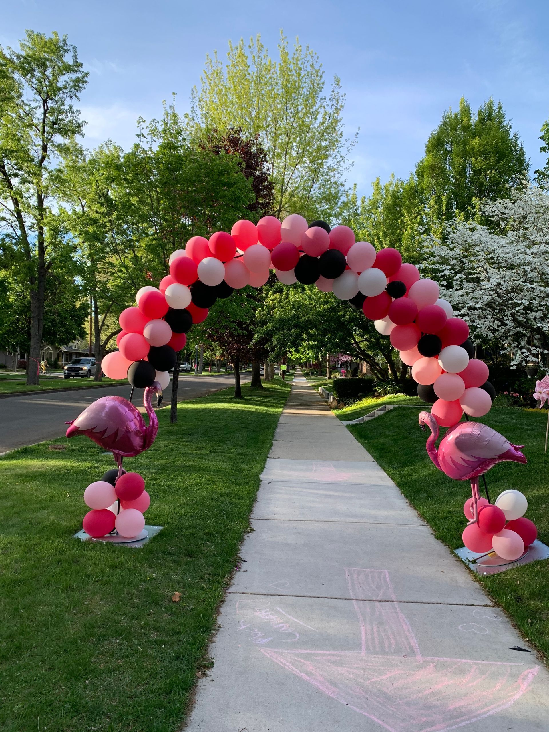 A pink and black balloon arch is sitting on the side of a sidewalk.