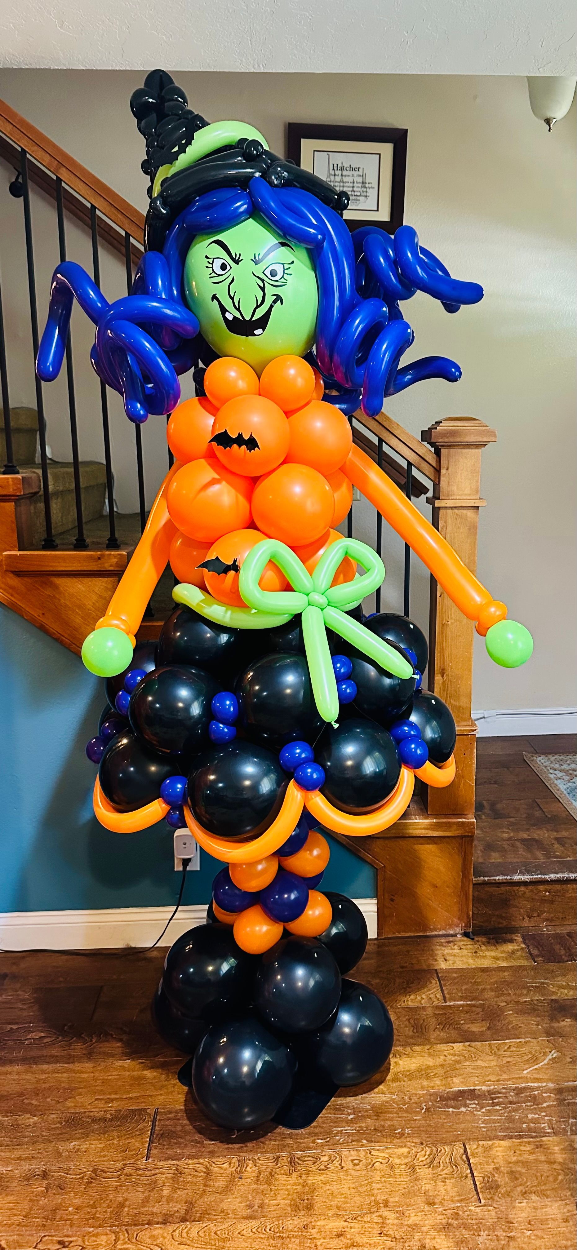A witch made out of balloons is standing in front of a staircase.