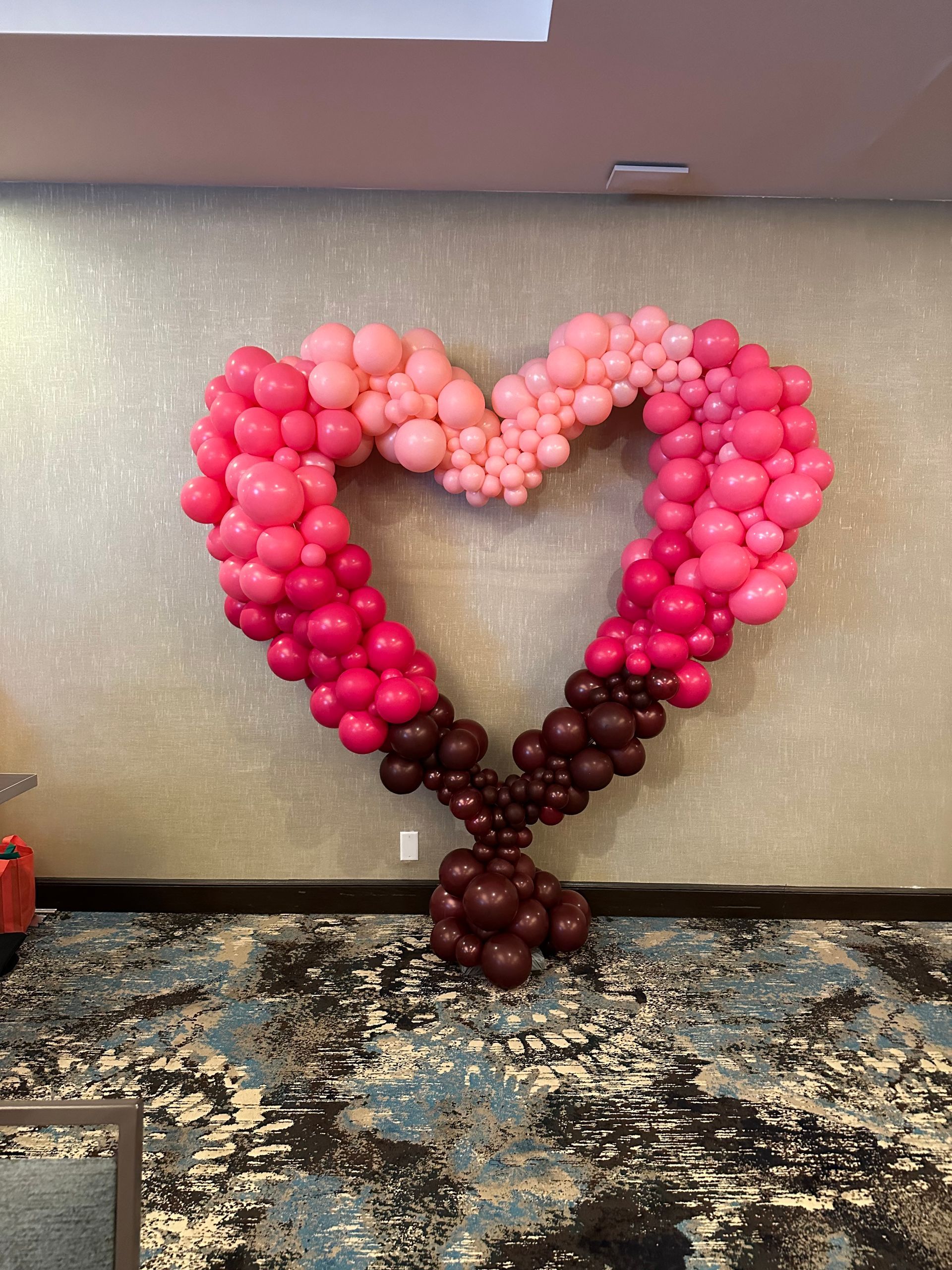 A large heart made of pink and brown balloons on a wall.