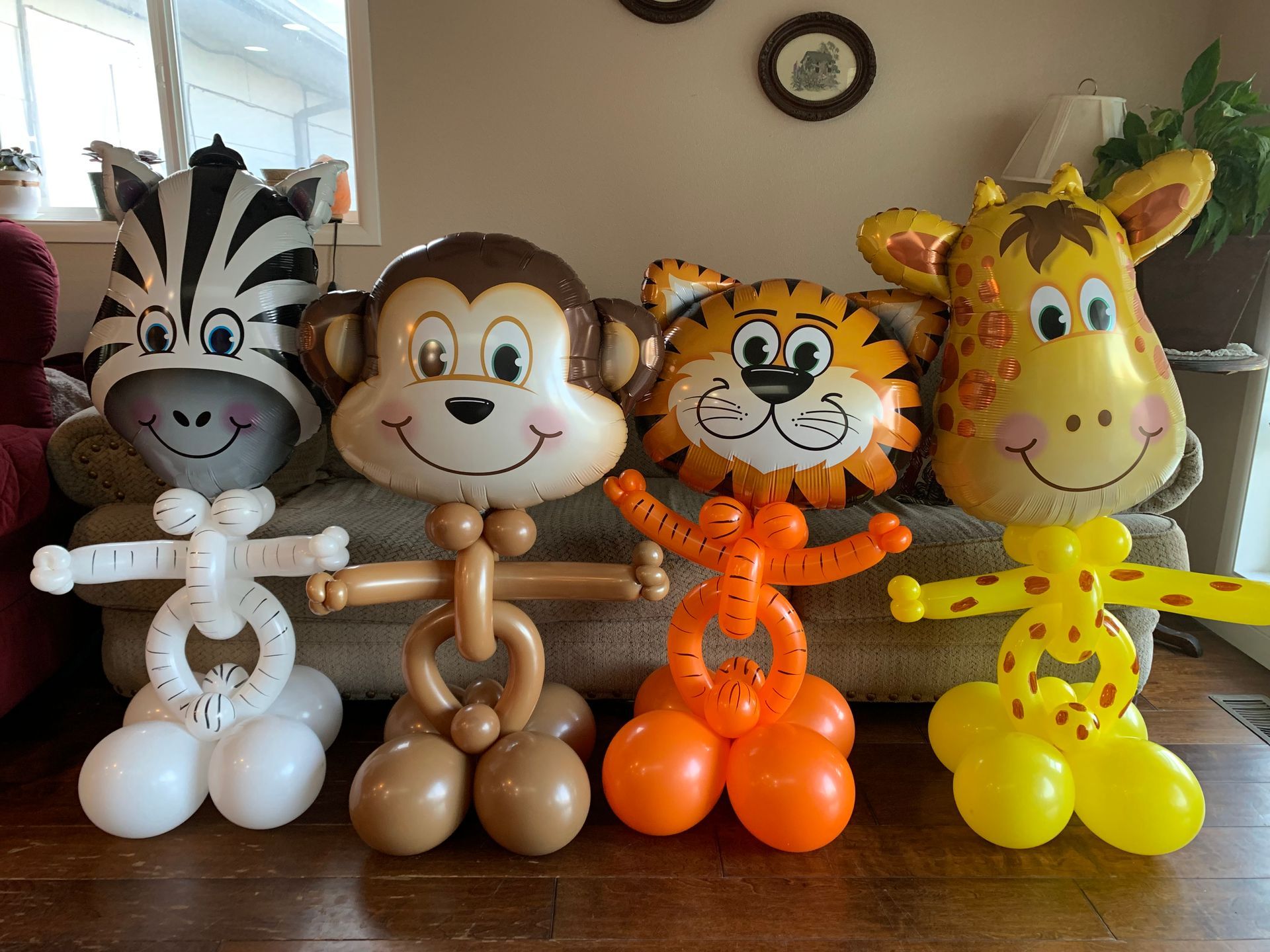 A zebra , monkey , tiger , and giraffe made out of balloons are sitting on a couch.
