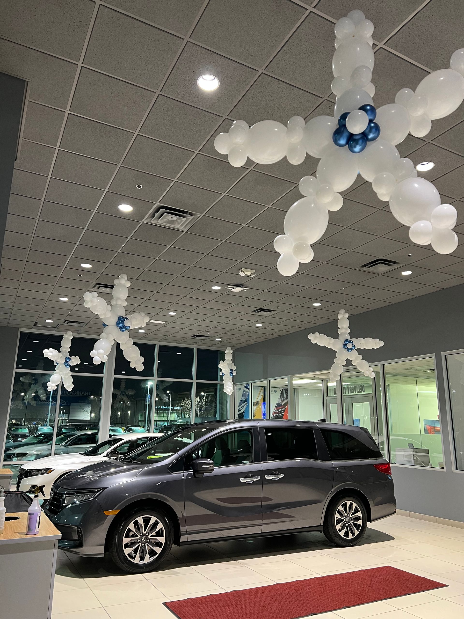 A van is parked in a showroom with balloons shaped like snowflakes hanging from the ceiling.