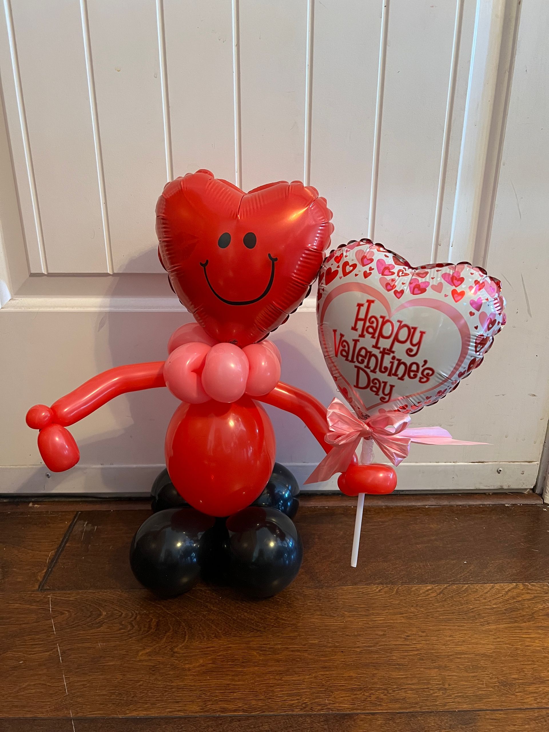 A red heart shaped balloon with a smiley face and a happy valentine 's day balloon on a stick.
