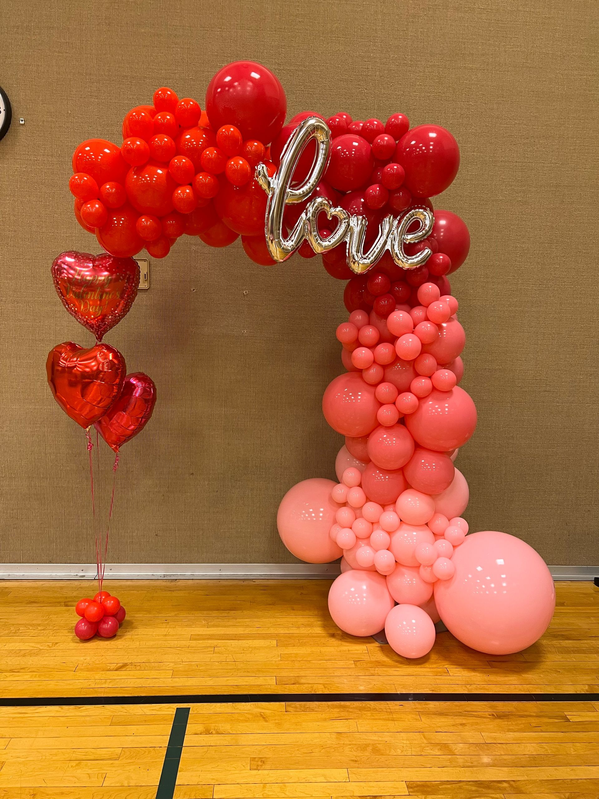 A balloon arch with the word love written on it is sitting on a wooden floor.