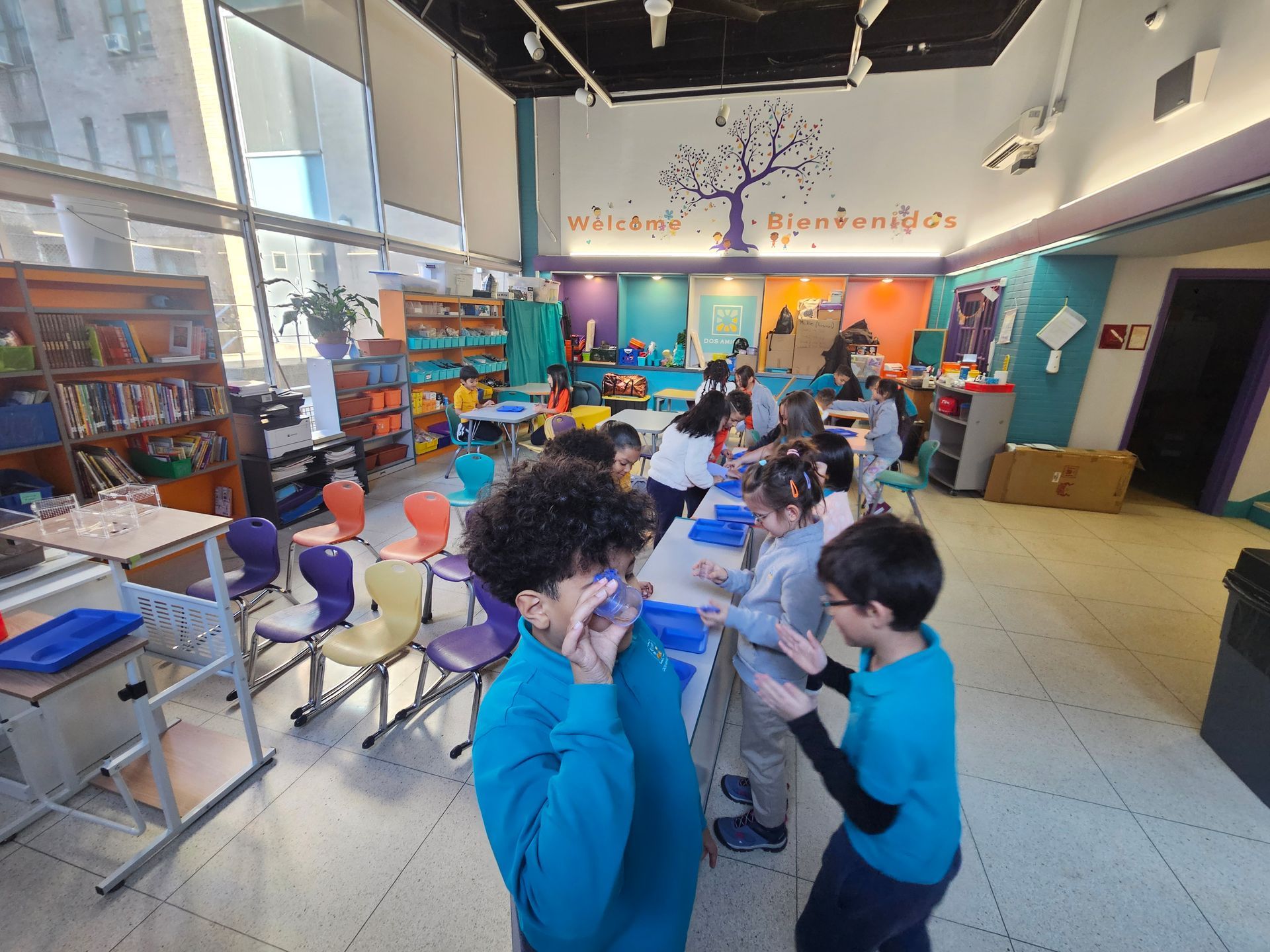 Children playing in a bright classroom with colorful decorations and desks.