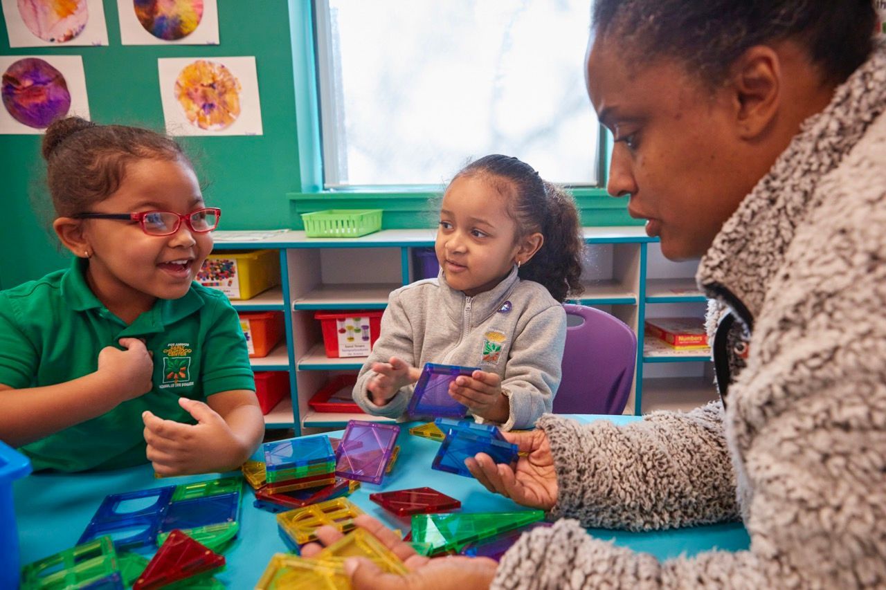 Three children playing with colorful blocks at a table in a classroom