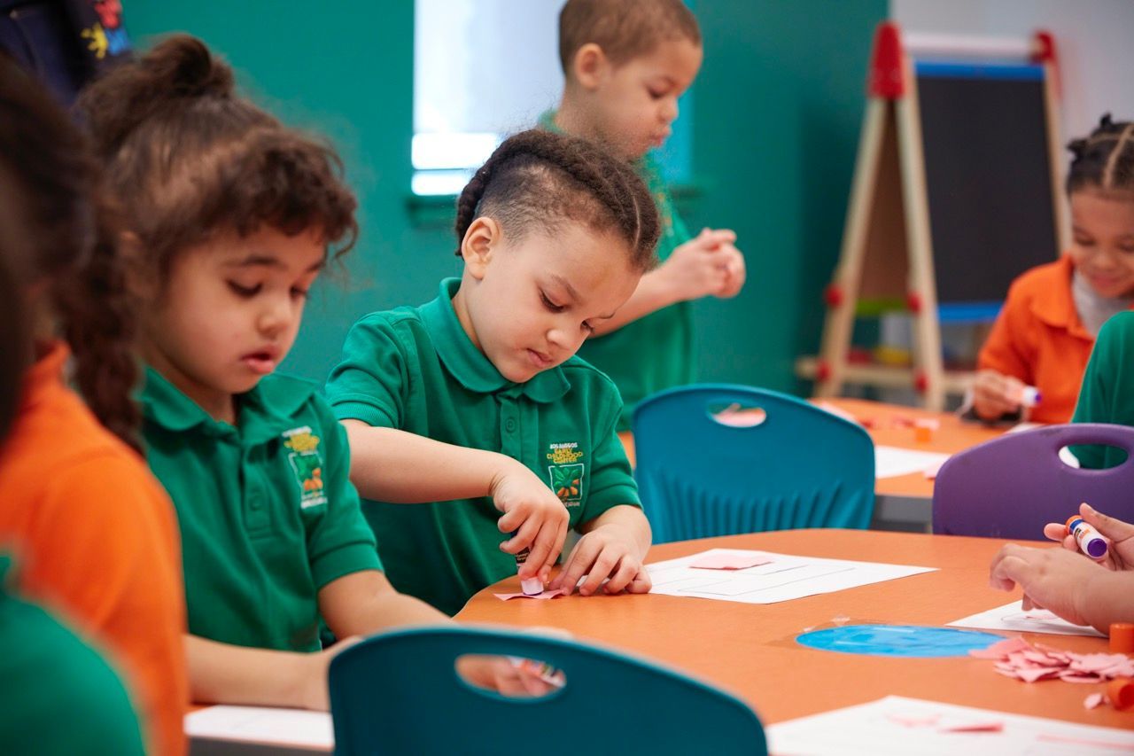 Children in green uniforms painting at a classroom table with bright art supplies