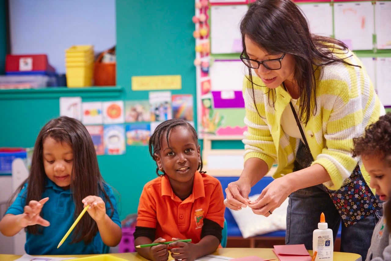 Teacher helping children with an arts and crafts activity at a colorful classroom table