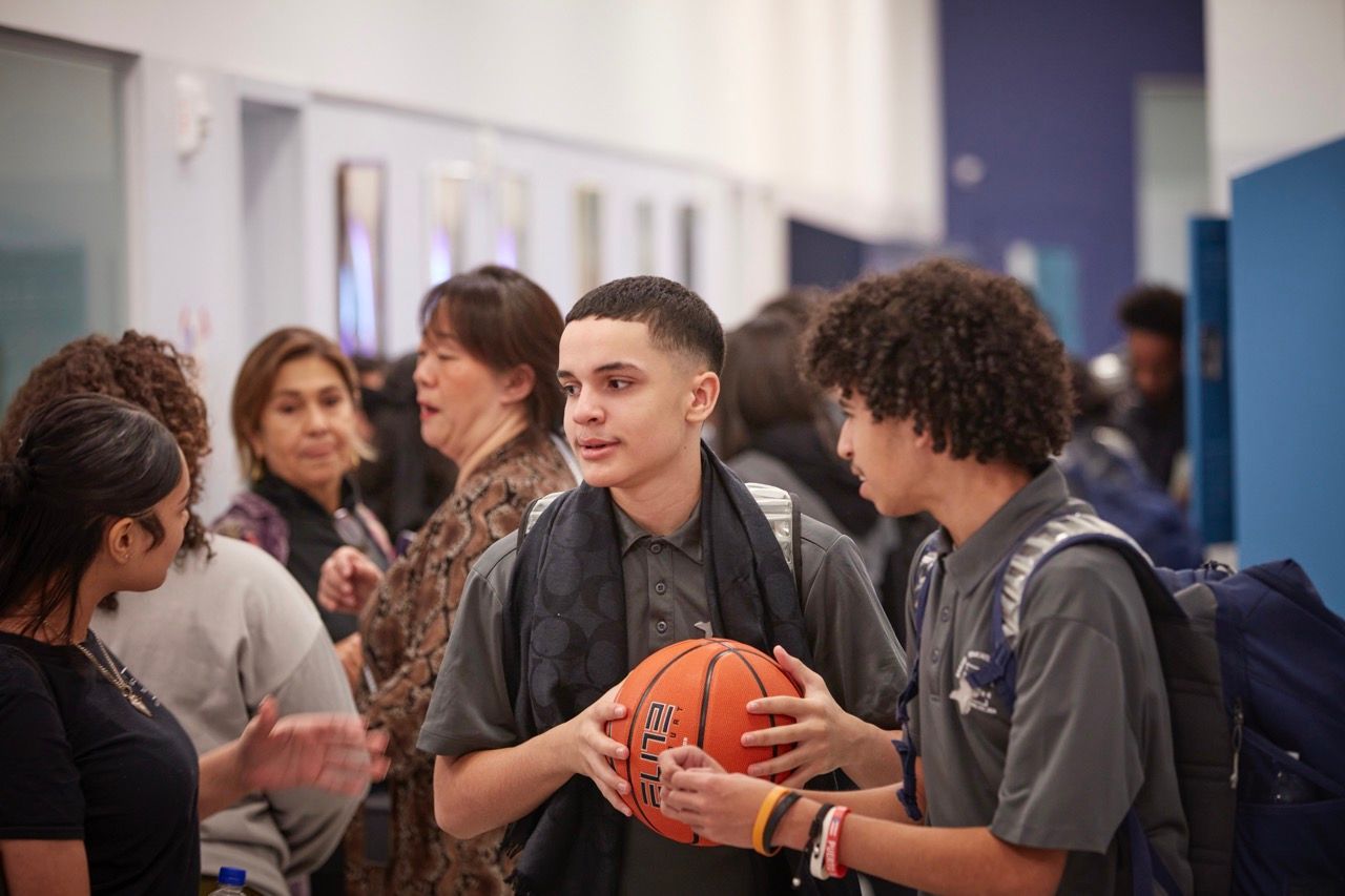 People chatting in a hallway, with one person holding an orange basketball.