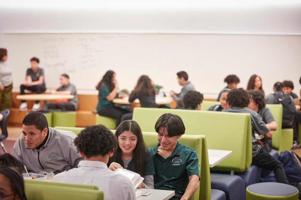 Students studying together in a bright classroom with tables and green seating booths