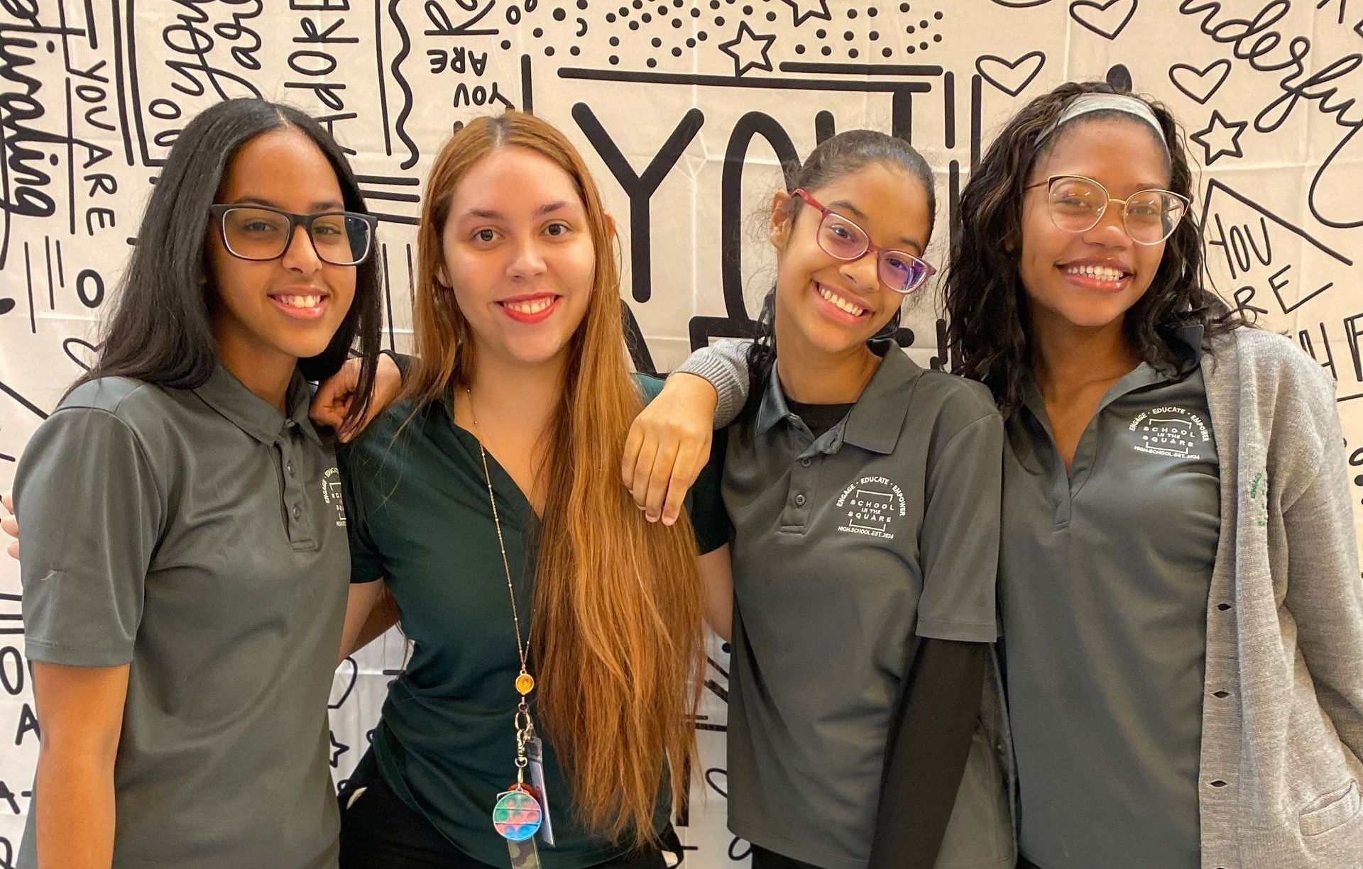 Four smiling students posing together in front of a graffiti-covered wall