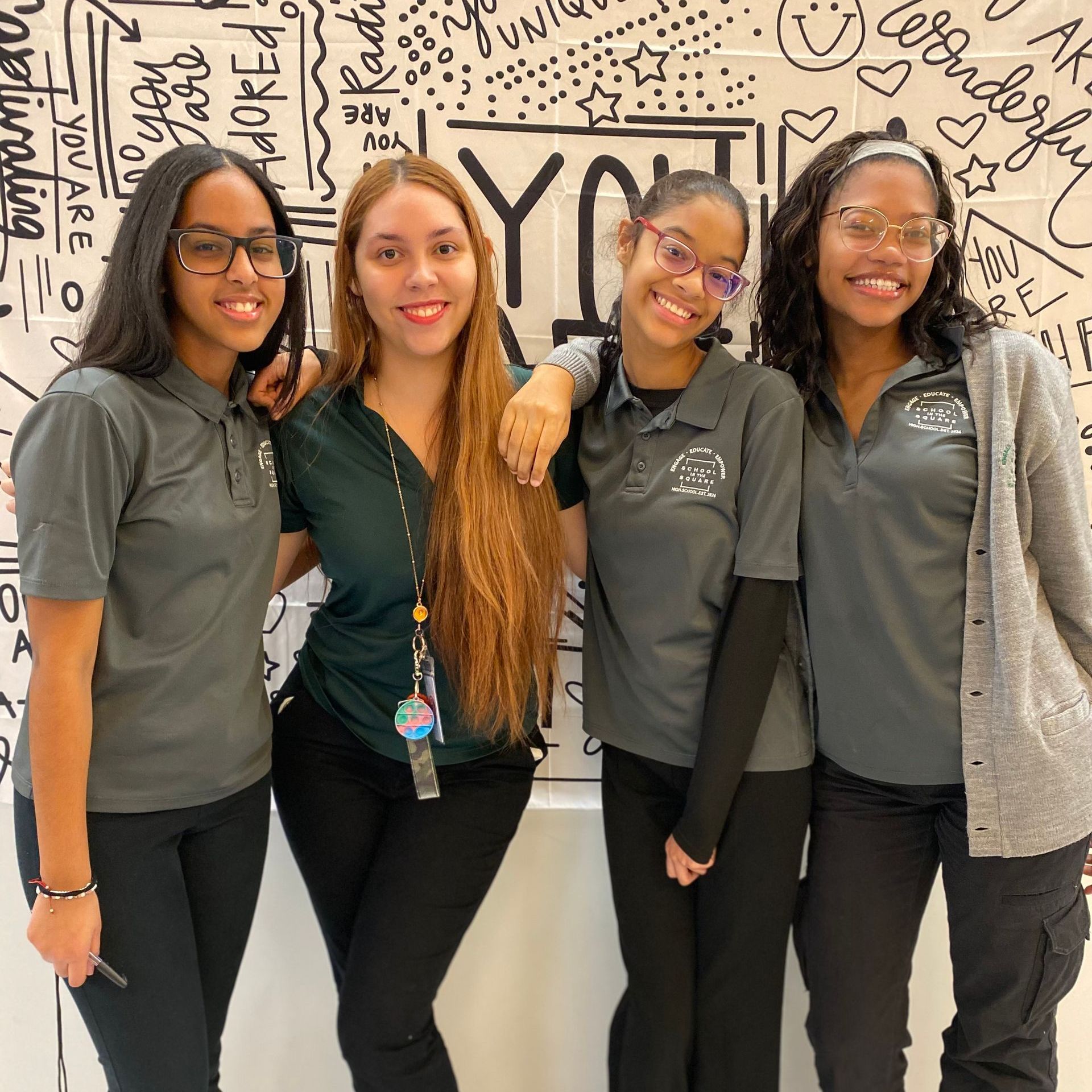 Four coworkers standing together, smiling in gray shirts in front of a graphic wall.
