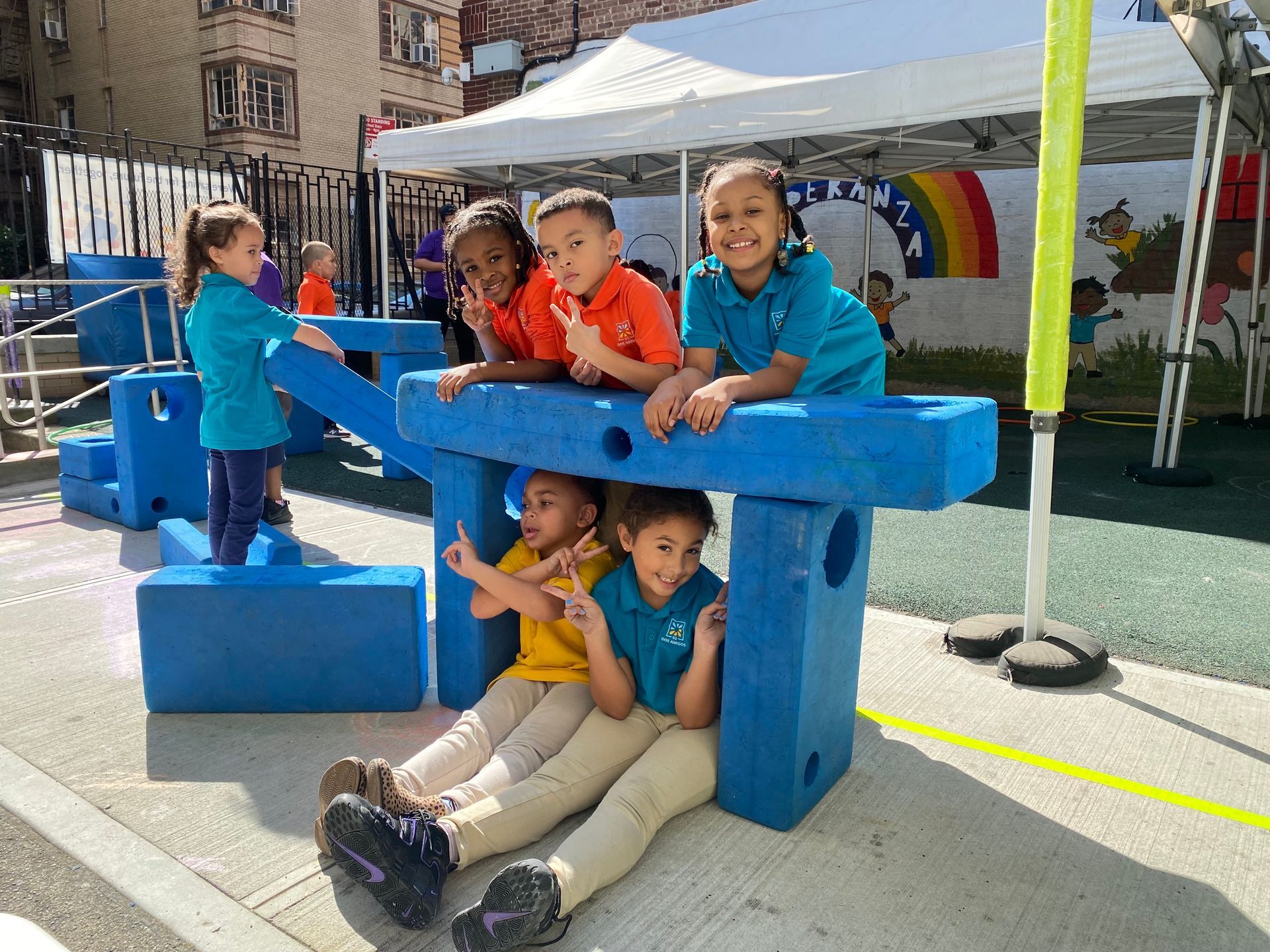 Children playing on a blue wooden structure at an outdoor event under white tents.