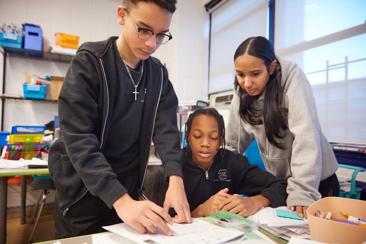 Students working together at a table with papers and art supplies in a classroom
