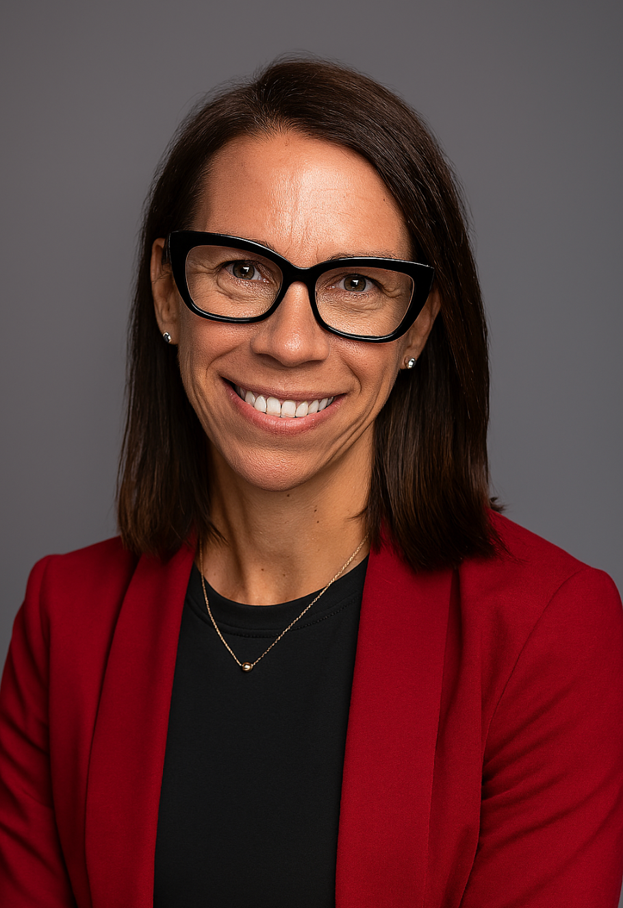 Monica Merchant headshot, wearing a red blazer on a gray background.