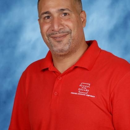 Noel Torres in a red polo shirt smiling against a blue studio backdrop