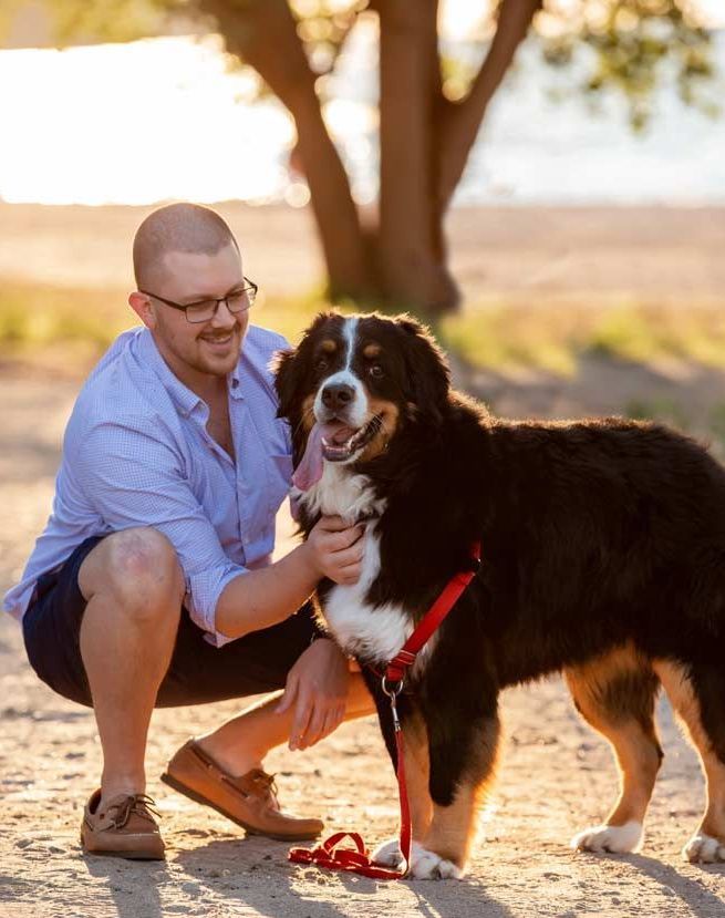 A man is kneeling down next to a large dog on a leash.