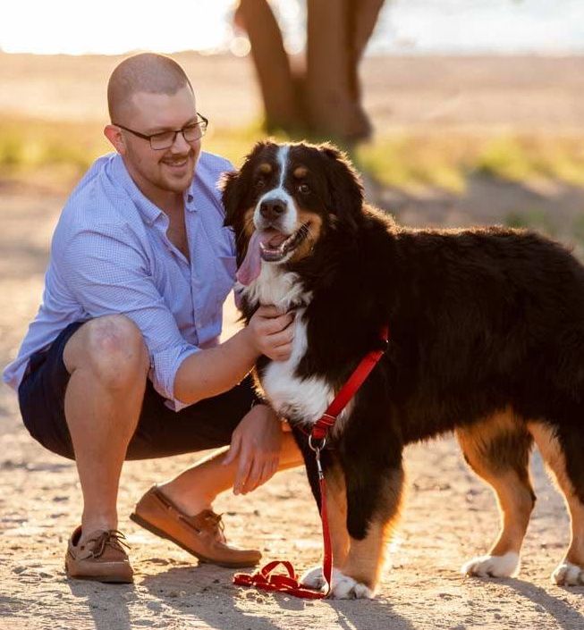 A man is kneeling down next to a dog on a leash