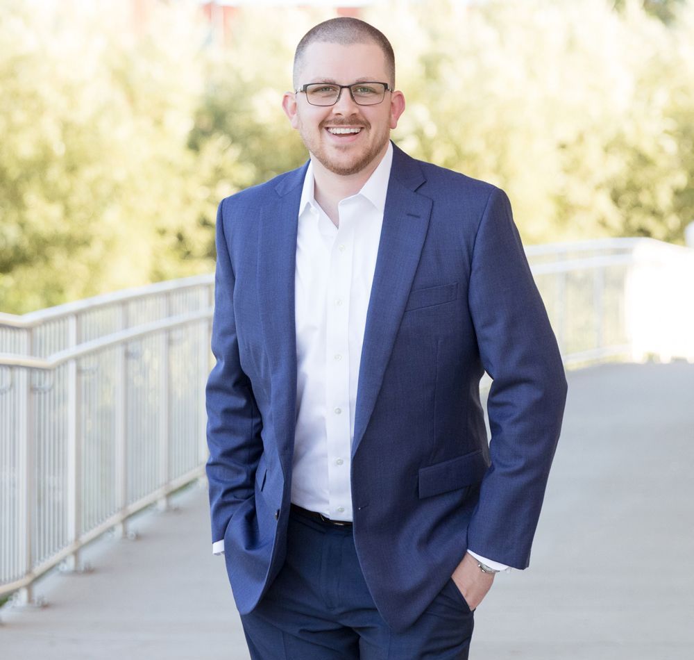 A man in a blue suit and white shirt is standing on a bridge with his hands in his pockets.