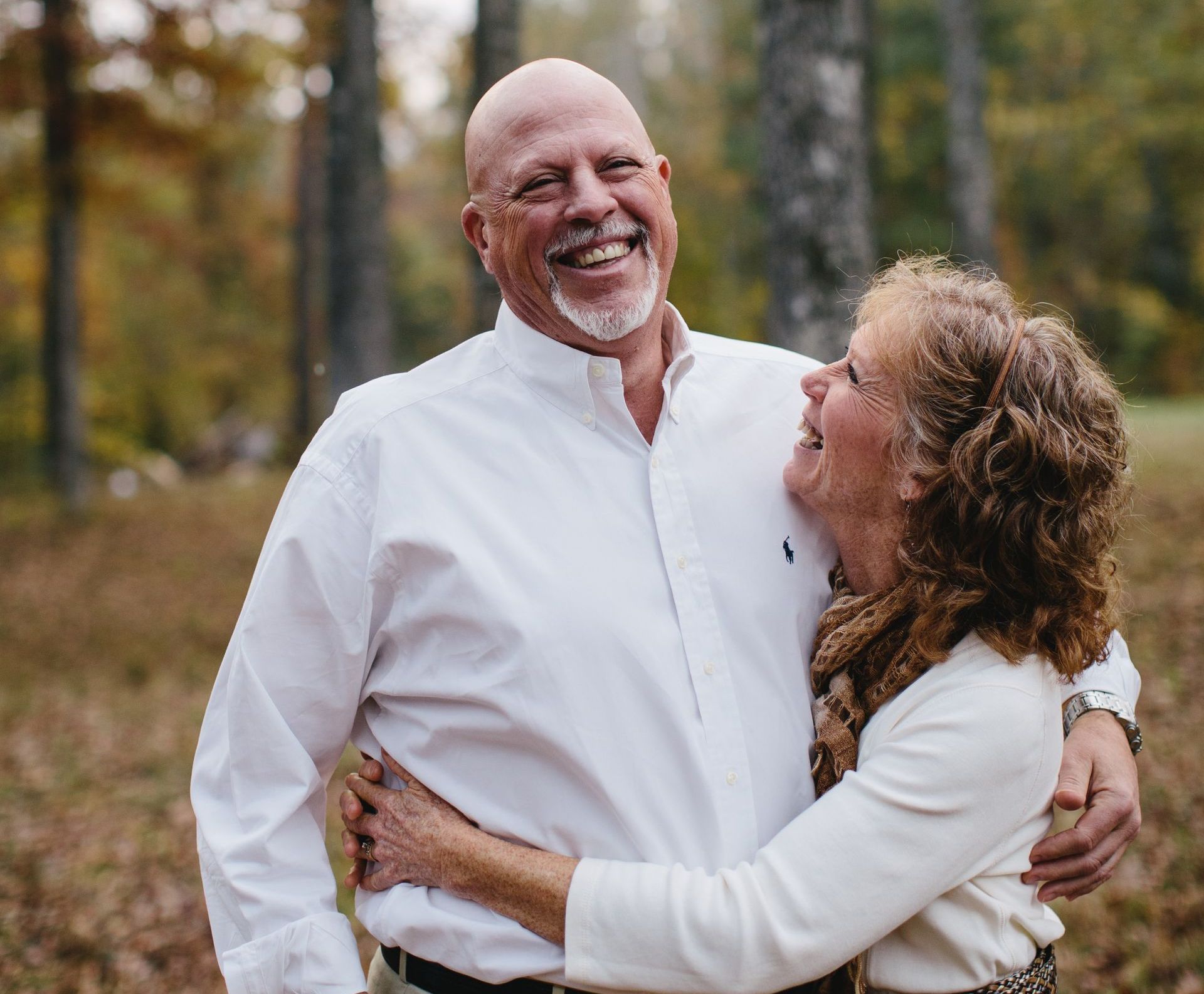 A man and a woman are hugging each other in the woods.