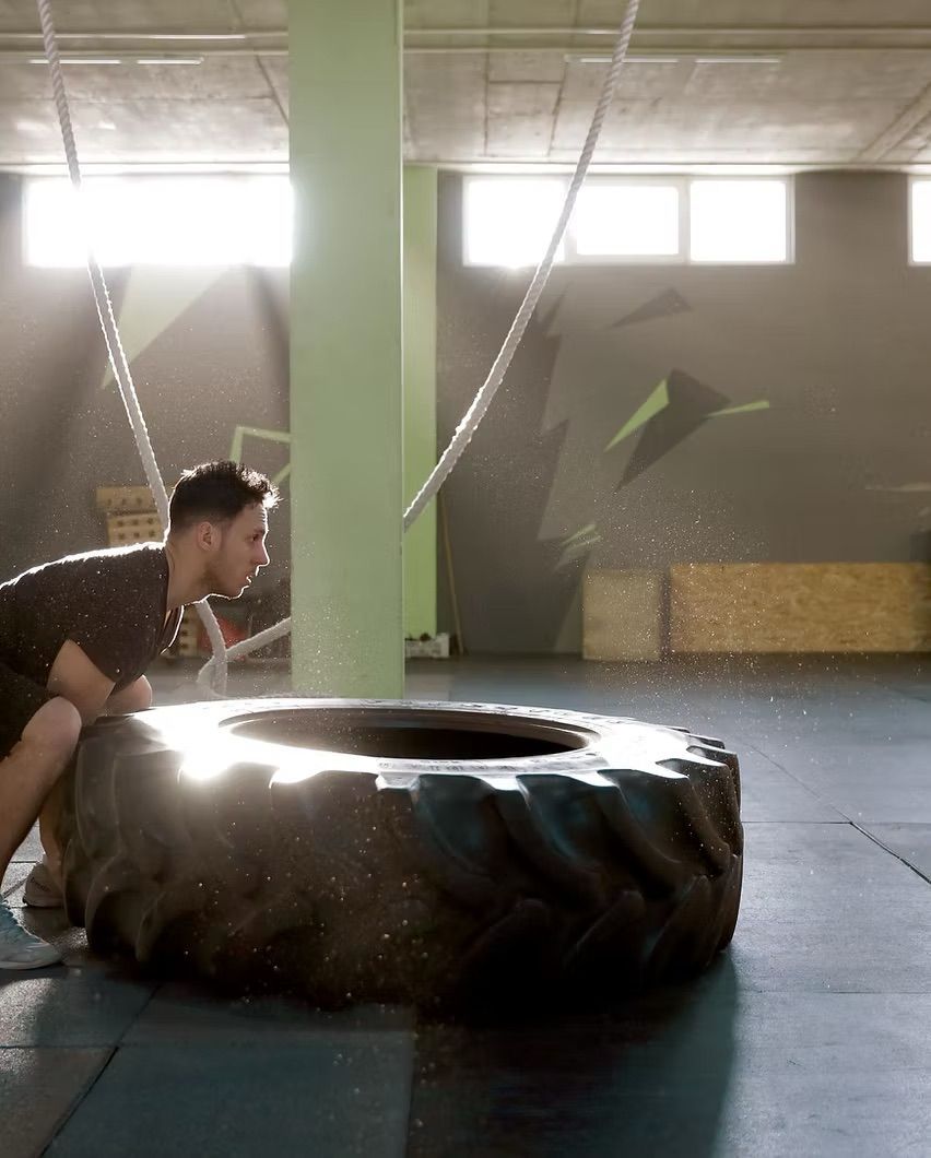 Person crouches beside a large tire in a gym, appearing to push or lift it during a workout.